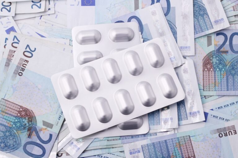 A person filling out prescription appeal paperwork at a kitchen table with medication bottles and documents nearby.