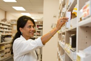 A pharmacy counter where a person hands a prescription and insurance card to a pharmacy technician.