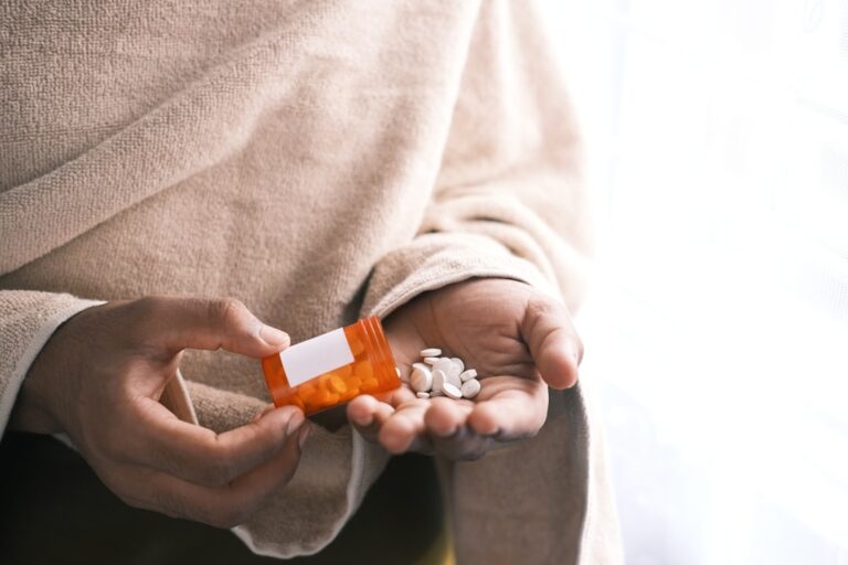 A senior couple at a kitchen table reviewing medication bottles and paperwork together.